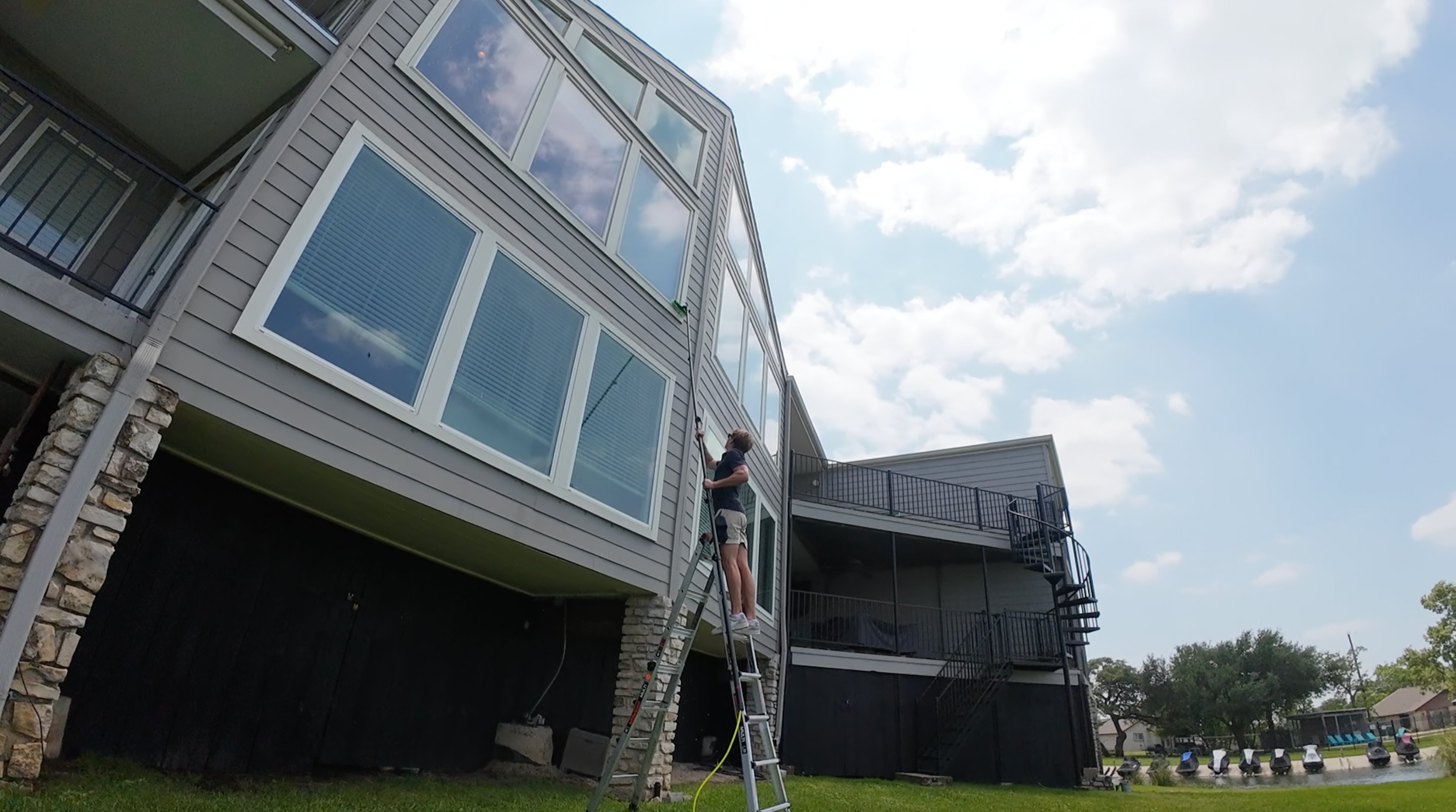 ClearCrew technician on a ladder cleaning a three-story wall of windows